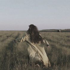 a woman walking through a field with her arms outstretched