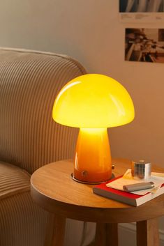 a yellow mushroom lamp sitting on top of a table next to a book and cup