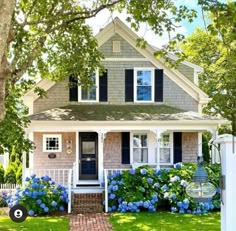 a white house with blue flowers in the front yard