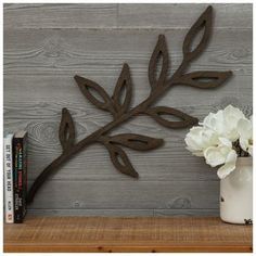 a metal branch with white flowers sitting on top of a wooden shelf next to a book