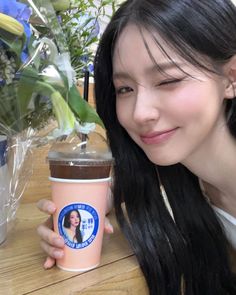 a woman holding up a coffee cup next to a vase with flowers in the background