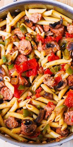 pasta with meat, peppers and mushrooms in a skillet on a wooden table next to utensils