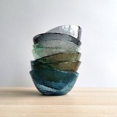 a stack of glass bowls sitting on top of a wooden table next to a white wall