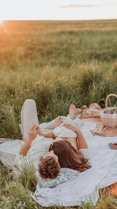 a woman laying on top of a white blanket next to a picnic table filled with food