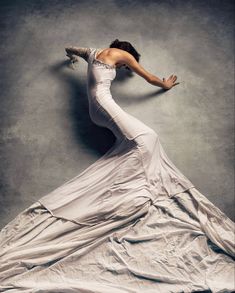 a woman in a long white dress is posing for the camera with her arms outstretched