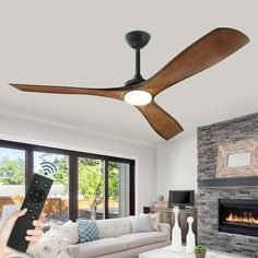 a person holding a remote control up to a ceiling fan in front of a fireplace