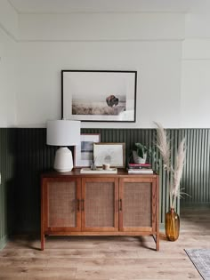 a wooden cabinet sitting in the corner of a room next to a lamp and pictures