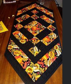 a quilted table runner with sunflowers and leaves on it, sitting on a wooden floor