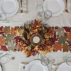 the table is set with white plates, silverware and autumn leaves on it's placemats