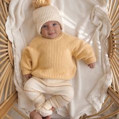 a baby wearing a yellow sweater and white pants with a pom - pom on it's head