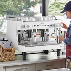 a woman standing in front of an espresso machine with cups on the side