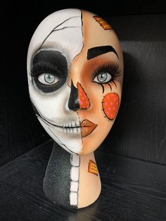 a woman's face painted with white and orange makeup on top of a black table