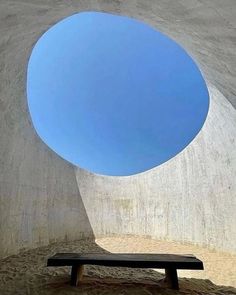 a bench sitting under a blue sky in a concrete structure with a circular window above it