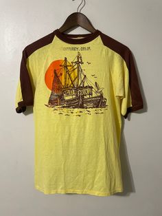 Vintage Monterey Shirt  - 80s vintage  - Two tone colour way  - Sailboat graphic  - Monterey California spell out  - Sunset design  Size: Medium (missing tag)  Good vintage condition  No rips or holes  No stains Vintage Souvenir Shirt, Retro Crew Neck Pre-shrunk Top, Vintage Crew Neck T-shirt With Front Print, Vintage Yellow Top With Retro Print, Vintage Cotton Crew T-shirt, Retro Cotton Crew Neck T-shirt, Vintage Cotton Crew Neck T-shirt, Retro Yellow T-shirt With Graphic Print, Yellow Retro T-shirt With Graphic Print