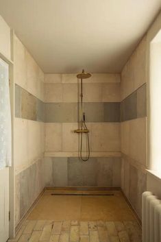 an empty bathroom with tile flooring and walls, shower head in the corner between two windows