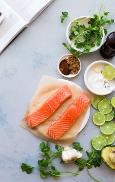 two raw salmon fillets on a plate with limes, avocado and other ingredients