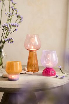 three different colored vases sitting on top of a table next to flowers and rocks