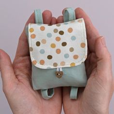 a hand holding a small purse with polka dots on the front and sides, it is in someone's hands