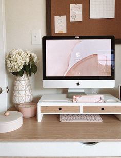 a desktop computer sitting on top of a wooden desk next to a vase with flowers