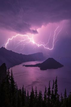 a large lake surrounded by mountains under a cloudy sky with lightning striking over the water