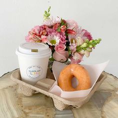 a donut, coffee cup and flower arrangement on a wooden tray with a marble table