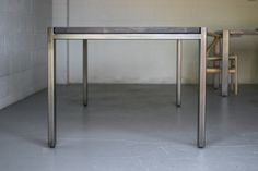 a table and two chairs in a room with white walls, concrete flooring and brick wall