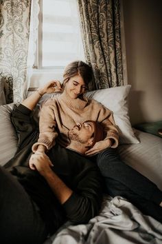 a man and woman sitting on top of a bed next to each other in front of a window