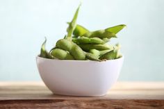 a white bowl filled with green beans on top of a wooden table