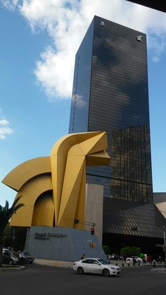 a large yellow sculpture in the middle of a parking lot next to a tall building