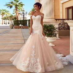 a woman in a wedding dress is standing on the sidewalk near some pillars and palm trees