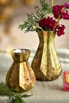 two vases with flowers in them sitting on a table next to candles and a candle holder