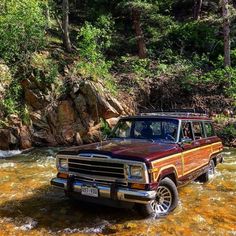 an old ford bronco is parked in the shallow water near some rocks and trees