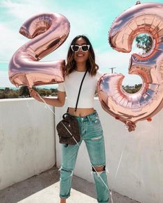 a woman in ripped jeans and white shirt holding up large pink balloons that spell out the number twenty