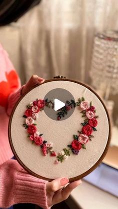 a woman is holding up a heart shaped embroidery project with flowers on it and the words love written in front of her