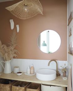 there is a sink in the bathroom with baskets under it and a round mirror on the wall