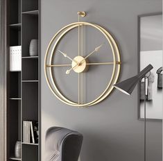 a clock is hanging on the wall next to a gray chair and bookshelf