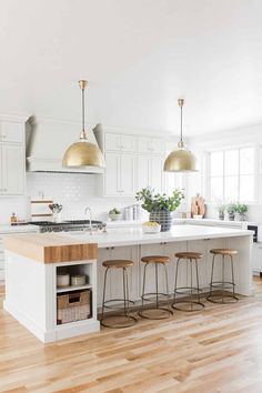 a kitchen with white cabinets and gold pendant lights hanging over the island in front of it