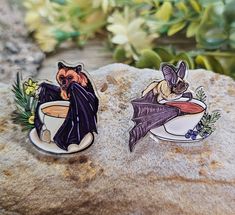 two pins with bats on them sitting on top of a rock next to some flowers