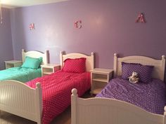 two beds in a room with purple walls and white headboards, one has a teddy bear on the bed