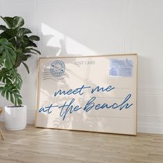 a sign that says meet me at the beach next to a potted plant on a wooden floor