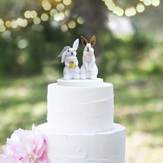 two small rabbits on top of a white cake