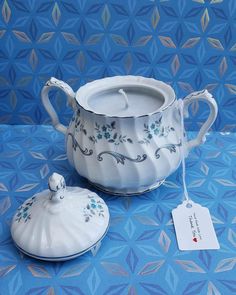 a white tea pot and saucer sitting on top of a blue cloth covered table