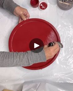 a person is painting a red object on a table with other items around it and the man is holding a paintbrush in his hand