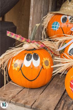 three pumpkins with faces painted on them are sitting on a wooden table and one has a straw hat