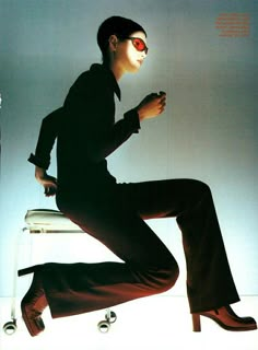 a man sitting on top of a chair next to a white wall and holding a cell phone