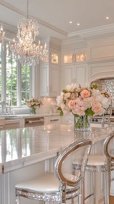 a kitchen with white cabinets and chandelier hanging from the ceiling, surrounded by glass stools