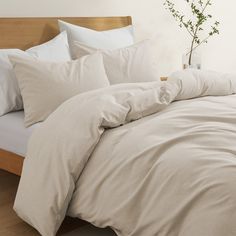 a bed with white sheets and pillows in a room next to a vase filled with flowers