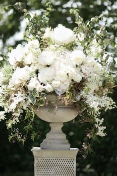 a vase with white flowers in it sitting on a table next to some bushes and trees