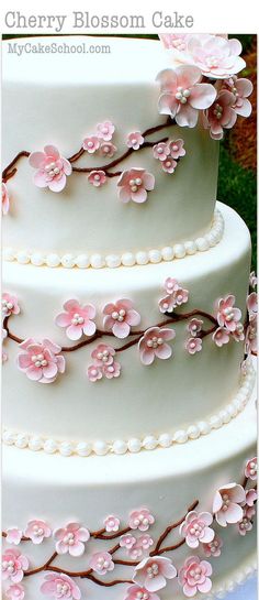 a three tiered white cake with pink flowers on the top and bottom layer is decorated with pearls