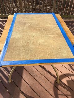 a table with blue tape on it sitting on top of a wooden deck next to a fence